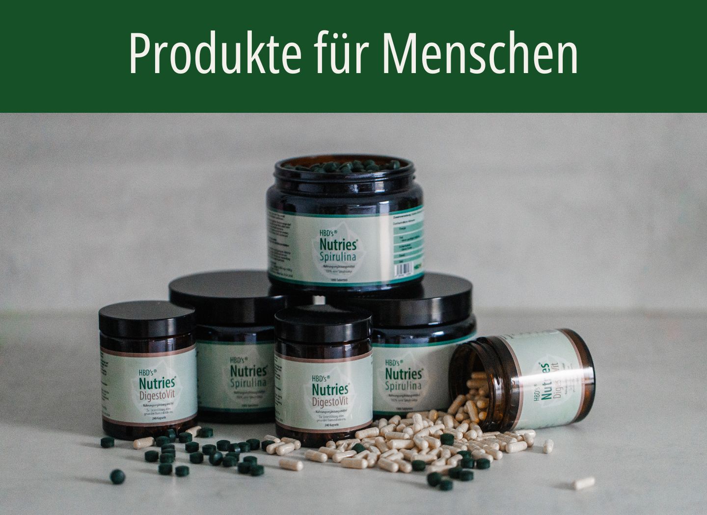HBD’s® Nutries® - Produkte für Menschen Die komplette HBD’s Nutries Produktlinie ist zu sehen. DigestoVit und Spirulina. Es liegen Kapseln und Presslinge um die Produkte herum.