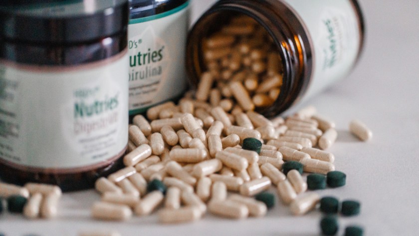 HBD’s® Nurties® - Nahrungsergänzungsmittel Ein Foto von mehreren Produkten der HBDs Nutries. Ein Glas liegt offen auf dem Tisch und es fallen mehrere Kapseln und Presslinge heraus.
