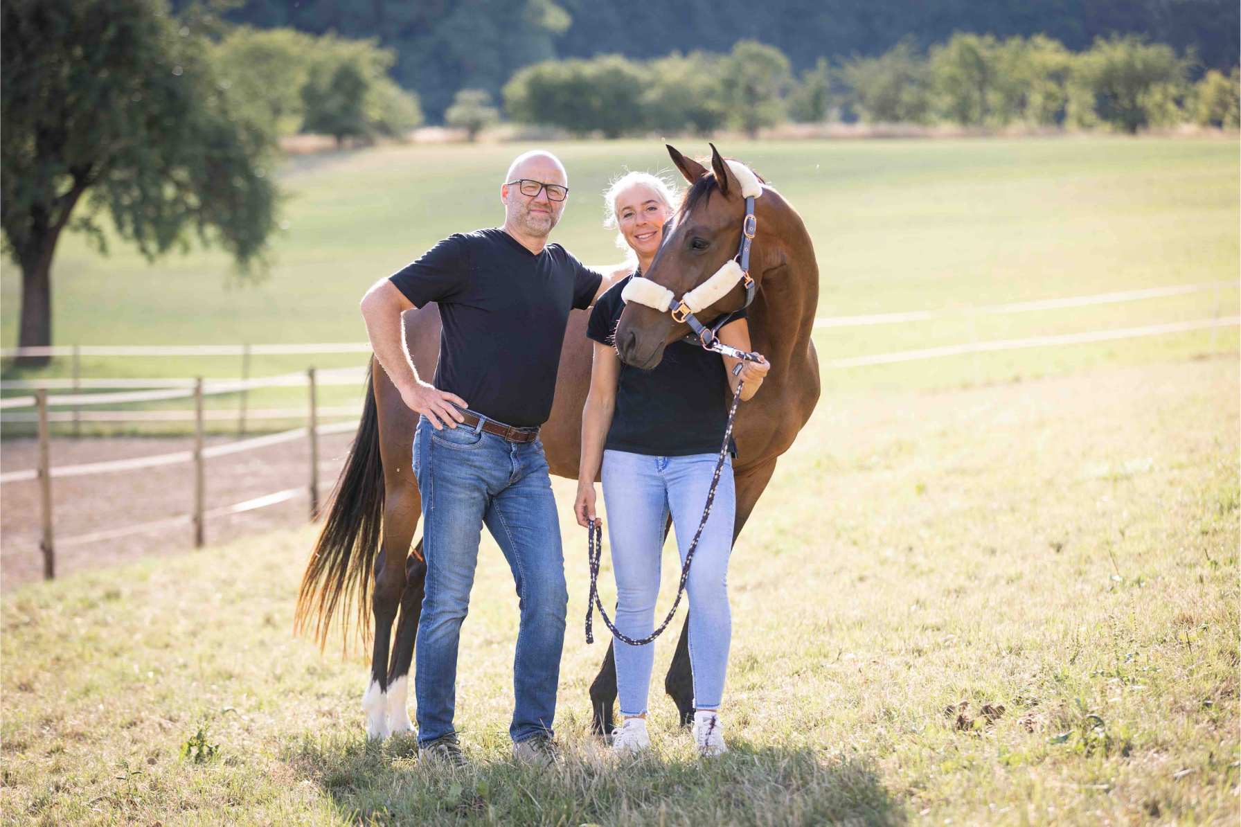 Heiner & Anja Beifuss Geschäftsführung HBD-Vital und HBD-Agrar Heiner und Anja Beifuss stehen zusammen mit einem braunen Pferd auf einer Weide bei sehr hellem Sonnenlicht