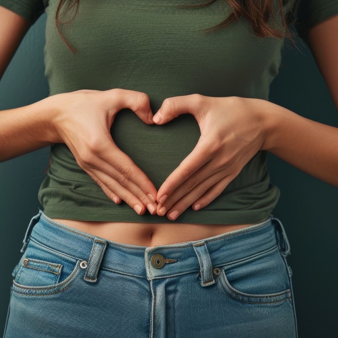 Eine Frau mit einem grünen T-shirt hält ihre Hände in Herzform vor ihren Bauch