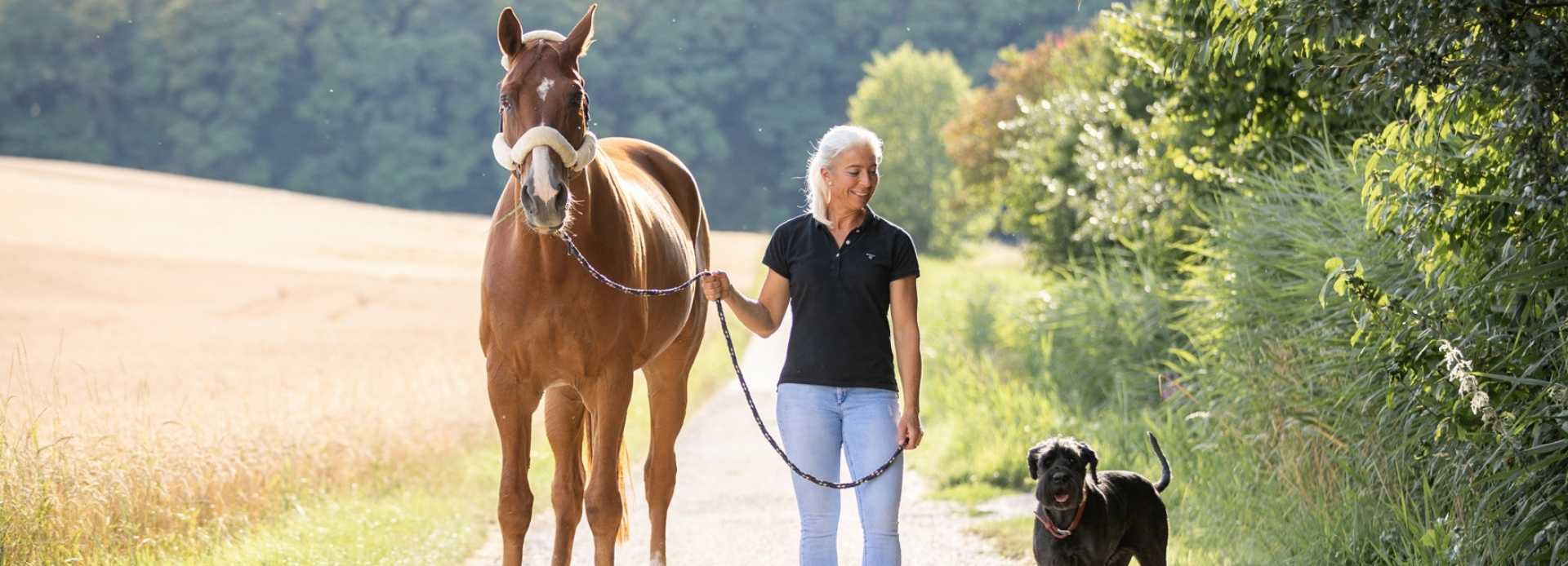 Anja Beifuss steht auf einer Straße mit ihrem Pferd und ihrem Hund.