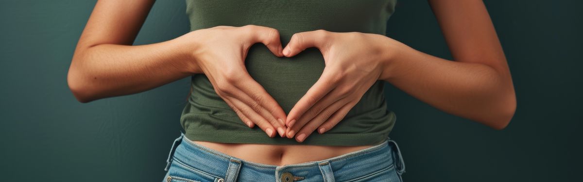 Eine Frau mit einem grünen T-shirt hält ihre Hände in Herzform vor ihren Bauch