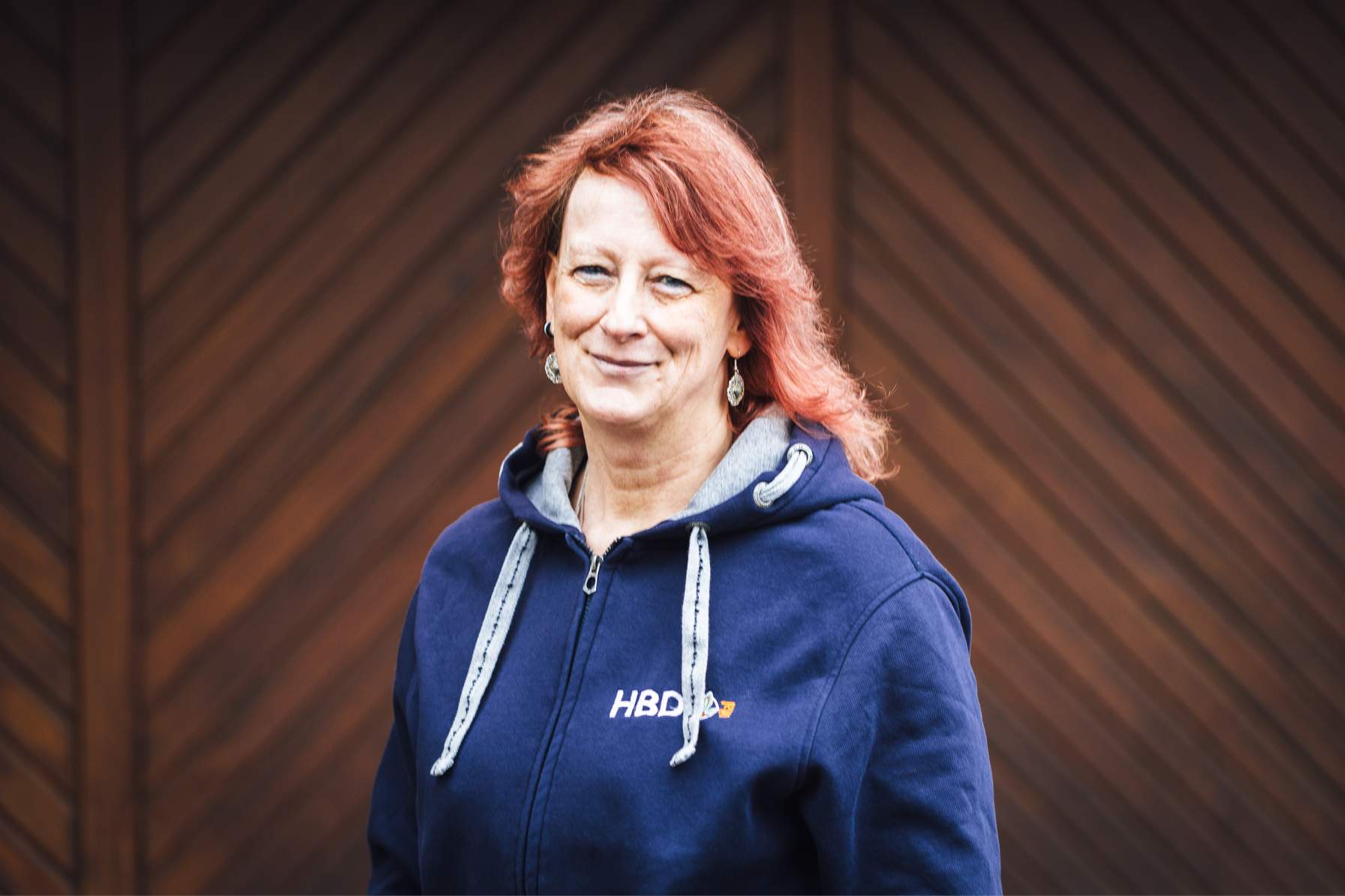 Frau Seidelmann Auftragverwaltung Frau Seidelmann aus der Auftragsverwaltung steht vor einem braunen Tor und hat einen blauen HBD-Hoodie an